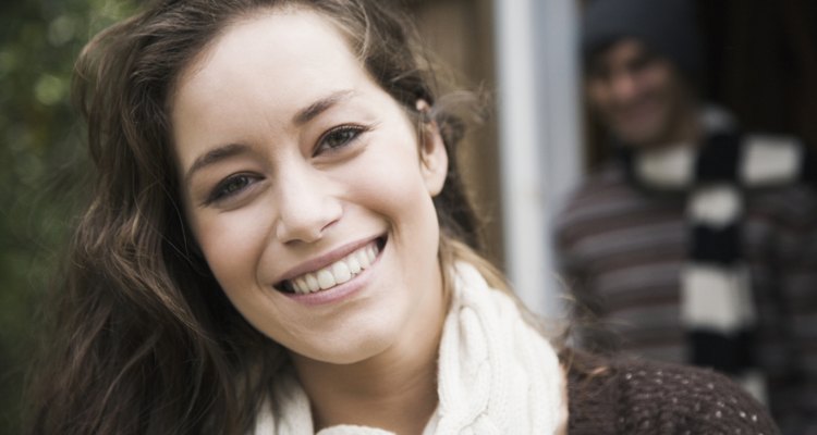 A close-up of a happy woman with a man smiling in the doorway behind her.