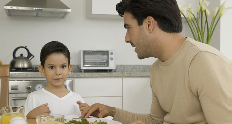 Man and boy sitting at table in kitchen, with salad and orange juice on table and man talking to boy, close-up