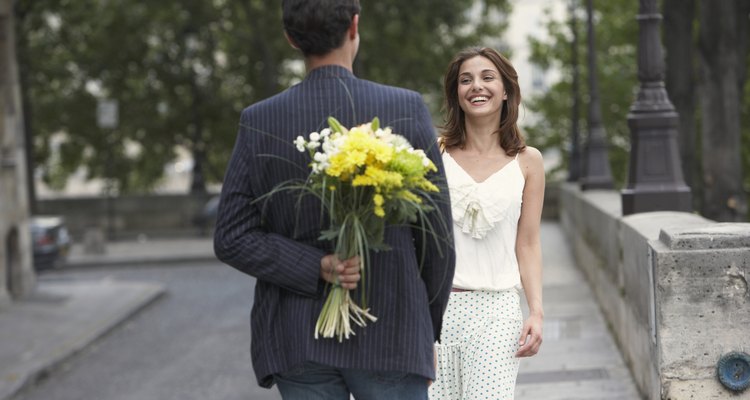 France, Paris, young couple outdoors, man holding flowers behind back