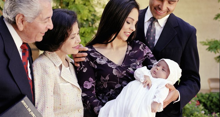 Family looking down at baby boy (0-3 months) in christening gown