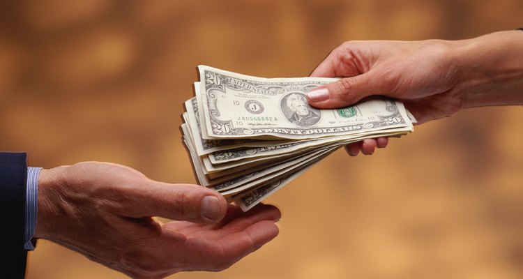 Woman's hand giving stack of US $20 bills to man's hand