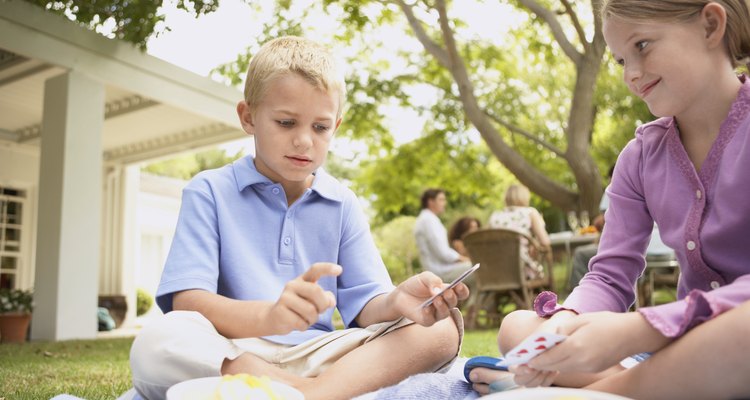 Young Boy and Girl Sit on a Rug in Their Garden, Playing a Card Game