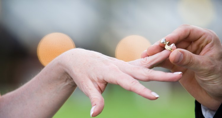 Man placing wedding ring on woman's finger outdoors