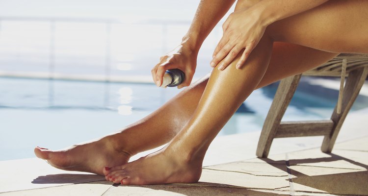 Woman spraying suntan lotion onto her leg by the pool