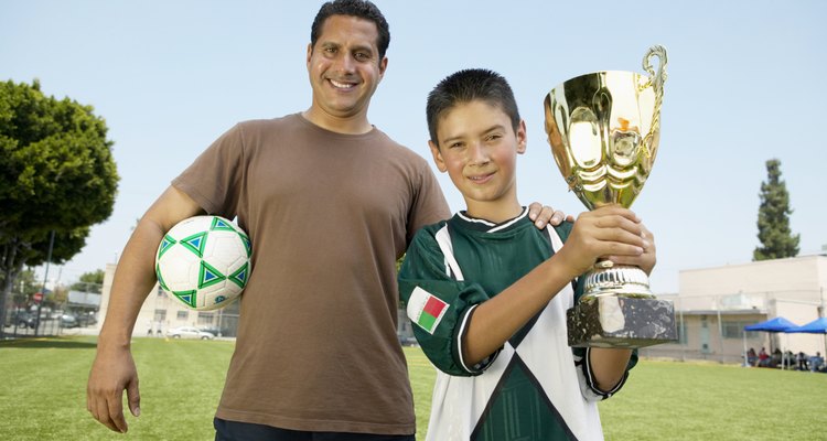 Father's hand on son's (7-9) shoulder, boy holding trophy, portrait