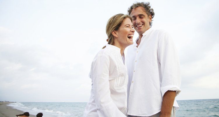 Couple standing on beach, smiling, children (7-9) in background