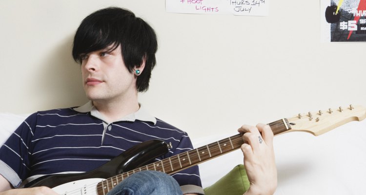 Man sitting on bed playing electric guitar