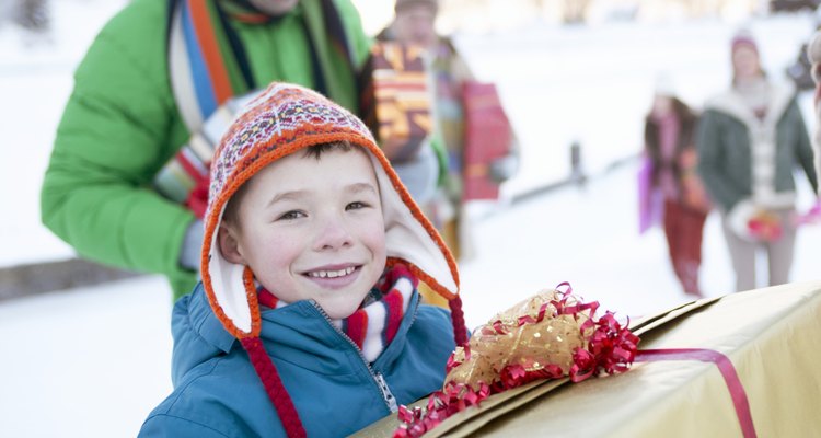 Boy (8-10) carrying present in snow, smiling, family in background