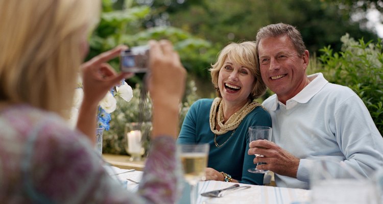 Woman taking photograph of couple at lunch table outdoors, smiling