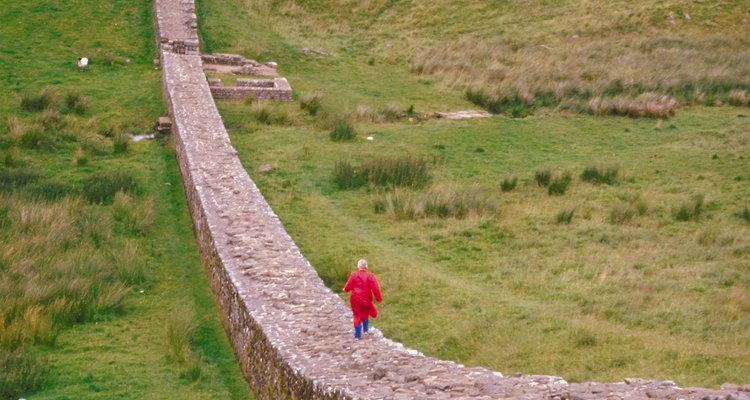 Hadrian's Wall and a walker that can't help herself hopping on top, despite warnings to protect the World Heritage site.