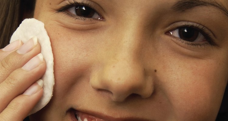 A headshot of a teen Caucasian female using a cleansing pad on her face while looking at the viewer