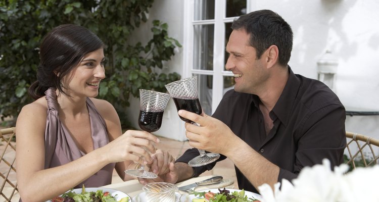 Couple toasting red wine at table, holding hands, smiling