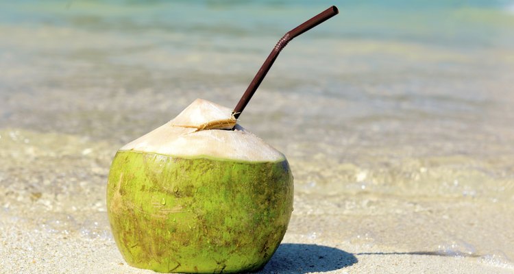 Opened coconut with a straw on summer beach.