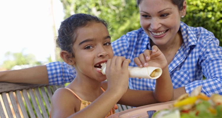 Girl (7-9) sitting at garden table with mother, eating tortilla wrap