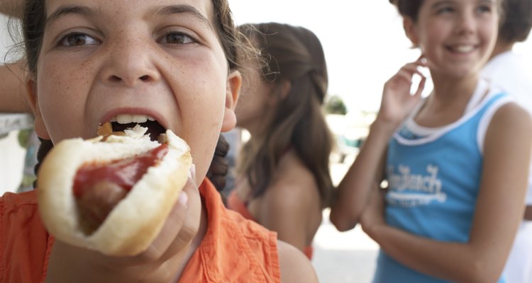Girl (7-9) eating hotdog, two girls (9-12) queuing in background