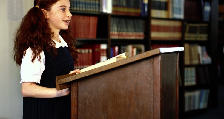 side profile of a school girl (8-10) reading from a podium in the library