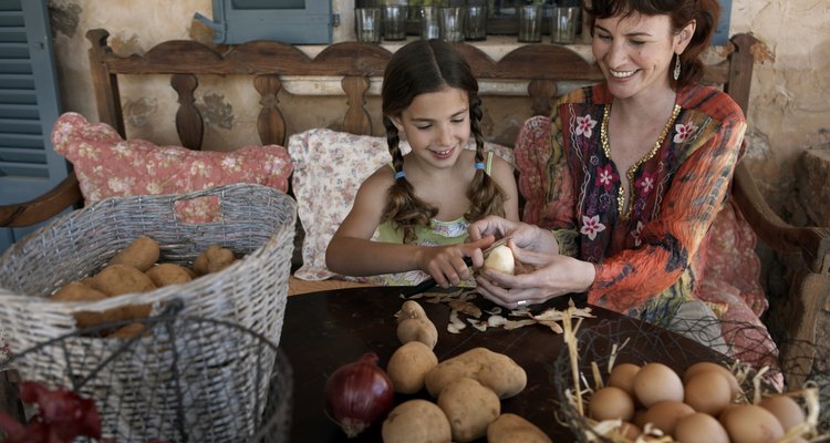 Mother and daughter (8-9) peeling potatoes on porch