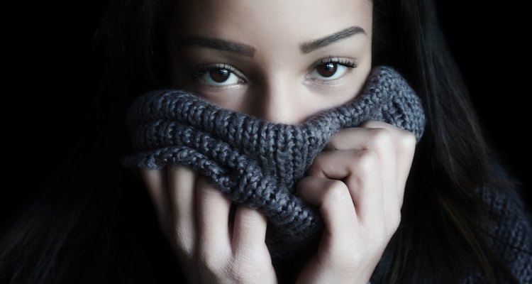 A young woman covers her face with a turtleneck, so that only the eyes and forehead are visible.
