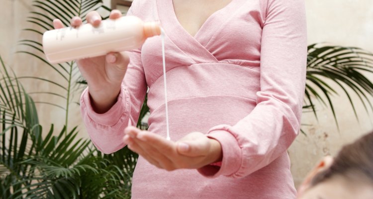 Young woman on treatment table, masseuse pouring lotion into palm