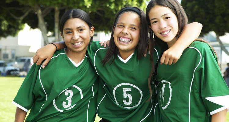 Female footballers (11-13) standing arm in arm, smiling, portrait