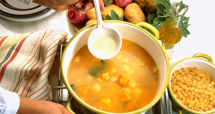 close-up of a hand stirring a bowl of soup cooking on a stove