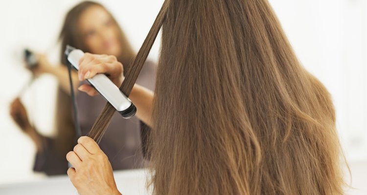 woman straightening hair with straightener . rear view