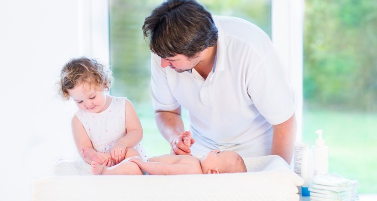 Adorable toddler girl helping father change diaper of her brother