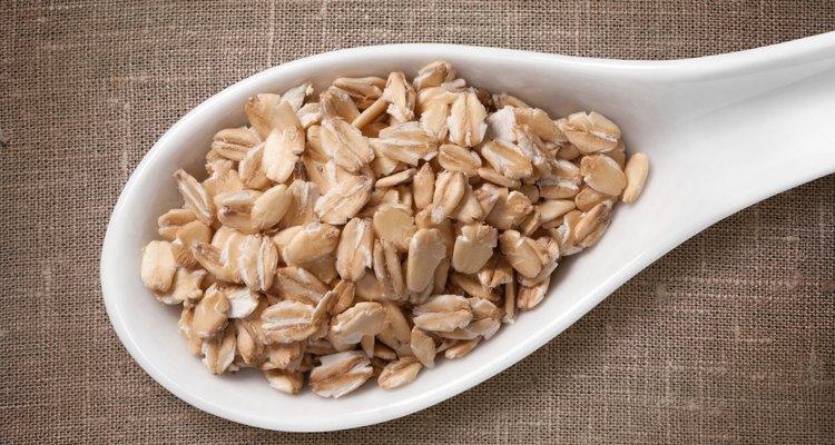 Rolled oats flakes in white porcelain spoon on sackcloth background