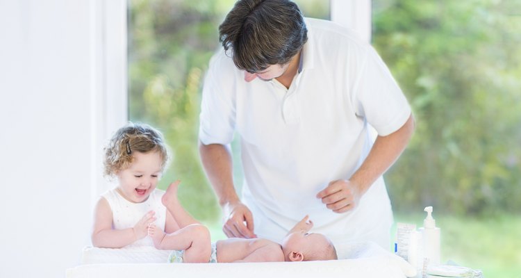 Newborn baby looking at his father and sister changing diaper