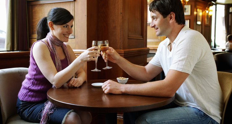 Couple sitting at table in bar, toasting with champagne, smiling