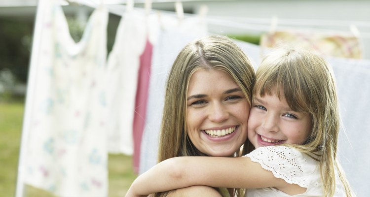 Mother and daughter (4-5) hugging by laundry line, portrait