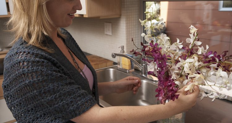 Woman arranging flowers in vase in domestic kitchen, side view