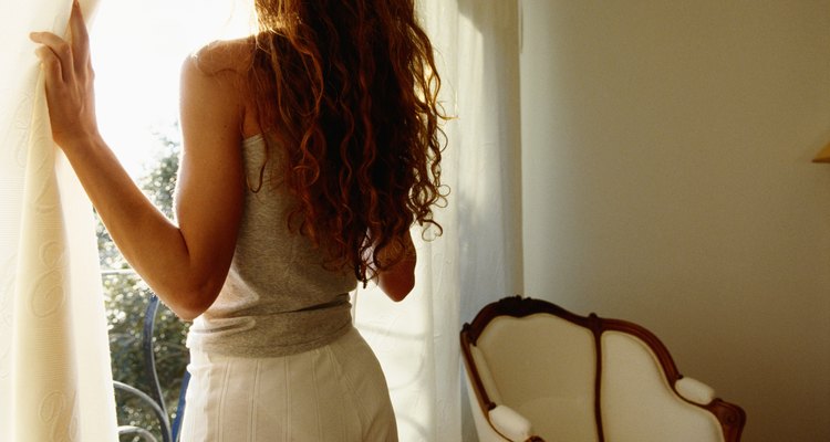 Young woman holding curtain, looking out window, rear view