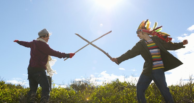 Teenage girl (16-17) and young man wearing feather headdress, duelling with sticks, side view