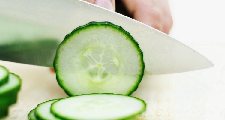 Close-up of a man's hand slicing a cucumber with a knife