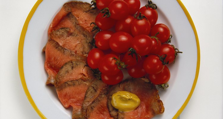 Slices of medium-rare roast beef shingled on a white plate with a side of fresh cherry tomatoes.