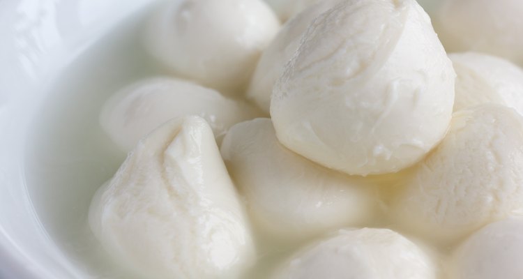 Small mozzarella balls in a white dish with liquid.