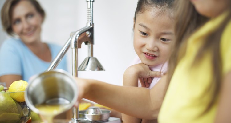 Girls (5-7) in kitchen pouring juice with woman in background