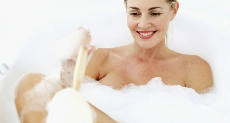 Young woman scrubbing her leg with a loofa in a bubble bath
