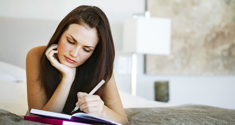 Young woman lying on a bed writing in a notebook