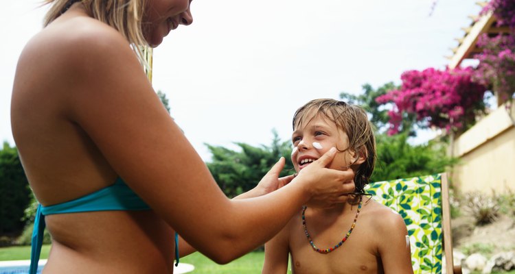 Mother applying sun cream to son's (8-10) face, smiling, close-up