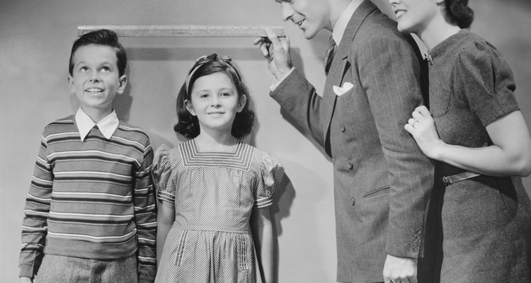 Parents measuring children standing against wall, boy (8-9) girl (6-7), (B&W)