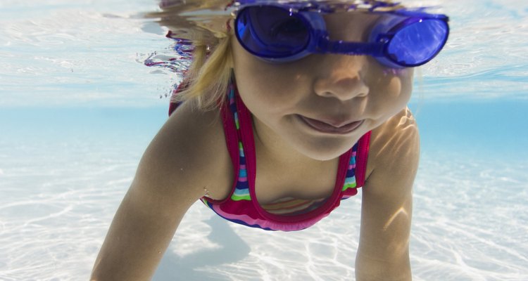 underwater lifestyle shot of a female toddler in goggles as she learns to swim in a pool