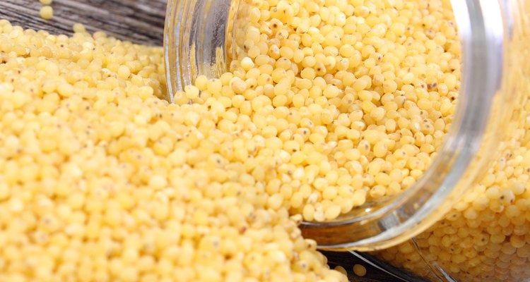 Millet groats spilling out of glass jar. Wooden background