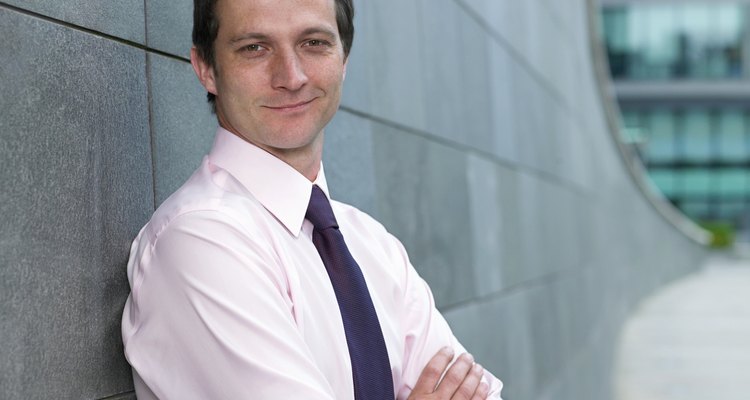 Businessman leaning against wall, arms folded, smiling, portrait