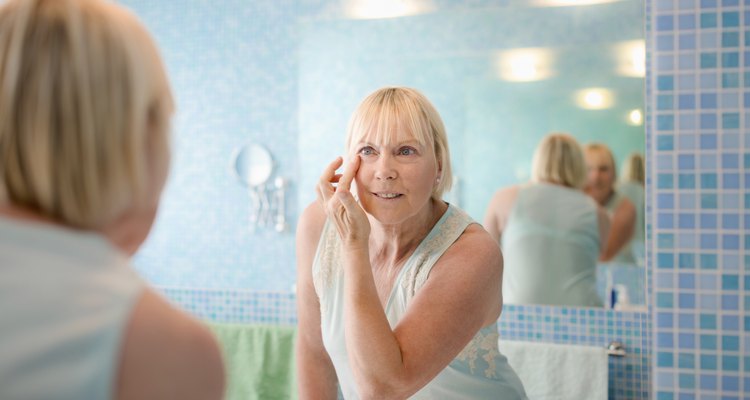 Female beauty, old woman applying cream on face at home