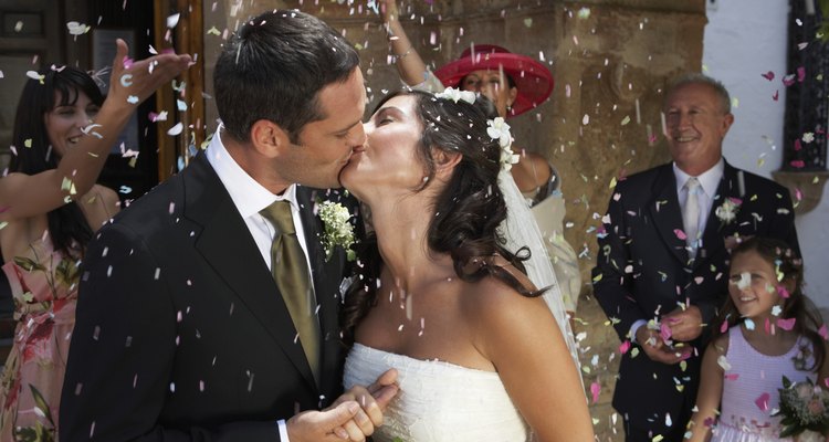 Guests throwing confetti over kissing bride and groom, outdoors