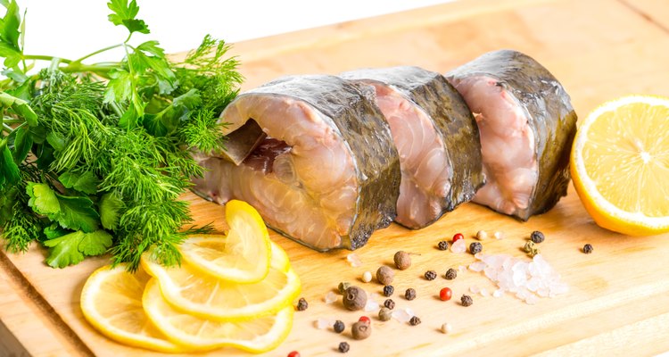 raw sliced steak of sturgeon fish with greens, lemon,