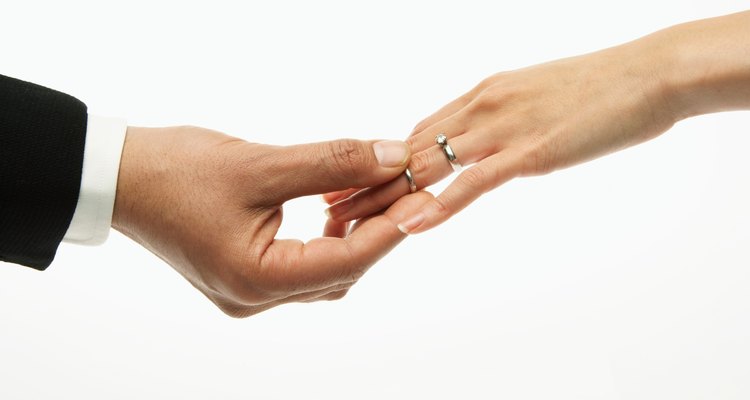 Man placing wedding band on woman's hand (focus on hands)