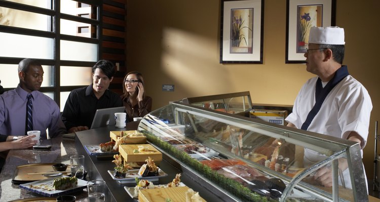 Group of people sitting in sushi bar, waiter behind counter, one man using laptop